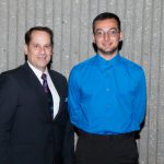 Man in a suit and tie smiling standing with a young man wearing glasses in a blue shirt,