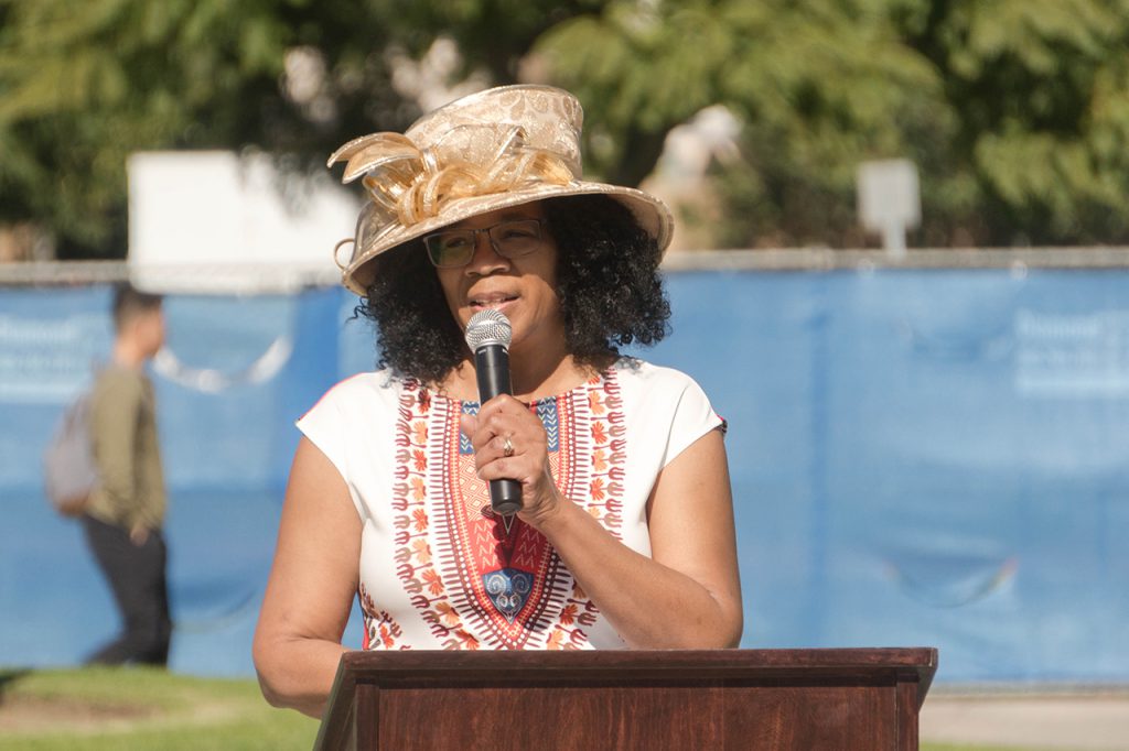 Woman with glasses and hat speaking at the podium.