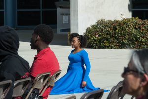 Girl in a blue dress sitting on the ground.