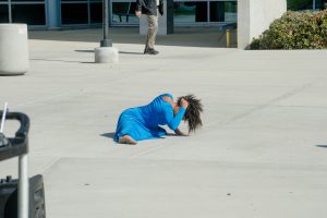 Girl in a blue dress on the ground doing a dance move.