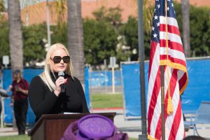 Woman with blonde hair and sunglasses speaking at the podium next to American flag.