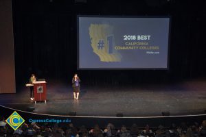 Gisela Verduzco speaking to an audience at the 2018 Connect2Cypress event with a large projector screen showing #1 2018 Best California Community Colleges.