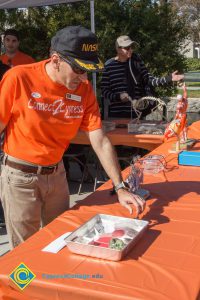 A man in an orange Connect2Cypress t shirt and a other man in a black and white striped shirt at a table with various displays.