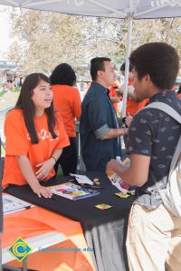 Students visiting and speaking with staff in orange t shirts at a Science, Engineering & Math booth.