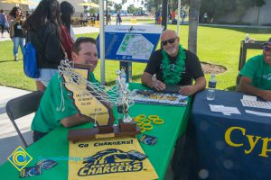 Three men sitting at a Cypress Charger Athletics information booth.