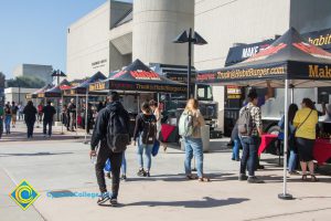 A row of Habit Burger food trucks and canopies with students walking and ordering food.