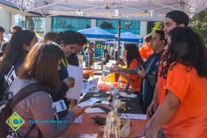 Students visiting and speaking with staff in orange t shirts at a Science, Engineering & Math booth.