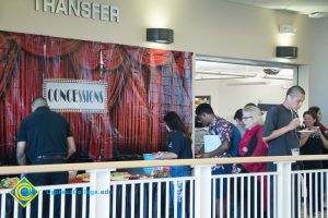 Students serving themselves food outside the Transfer Center with a red curtain design backdrop with a box that reads Concessions.
