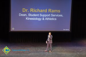 Dr. Richard Rams speaking on stage at the 2018 Connect2Cypress & Majors2Careers event with a large projector screen displaying his name and title behind him.