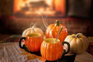 Pumpking mugs with hot drinks on a table with real pumpkins.